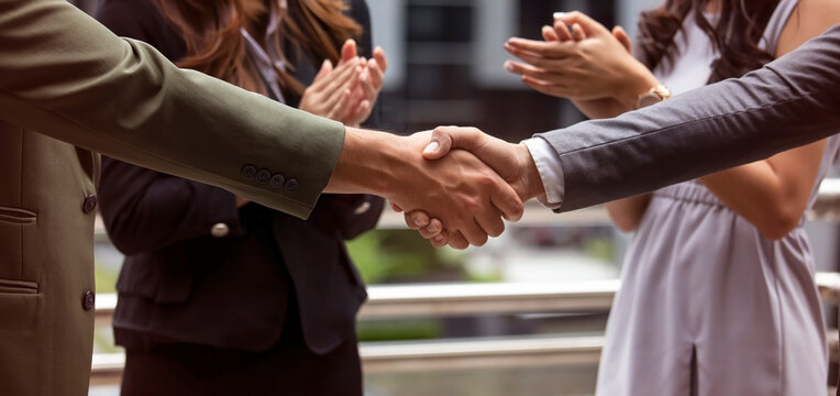 The celebrating business success and achievement with a handshake and deal agreement between two business partners with team clapping