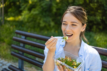 Woman enjoying a healthy vegan salad lunch on a park bench on a warm spring or summer day while waiting for a friend