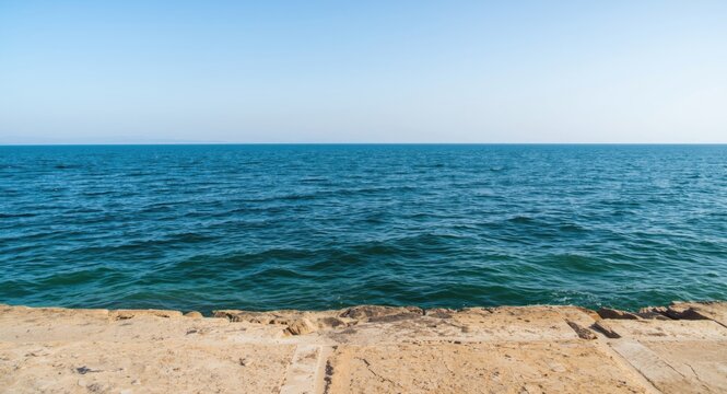Calm oceanfront panorama with flat rock surface and wave patterns beneath clear sky