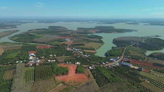 Aerial pan shot over colorful patchwork farmland surrounding Thac Mo Reservoir on a sunny day in Southern Vietnam.