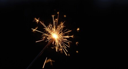 Fototapeta premium Intense close up of a glowing sparkler producing bright sparks in low light for festive occasions