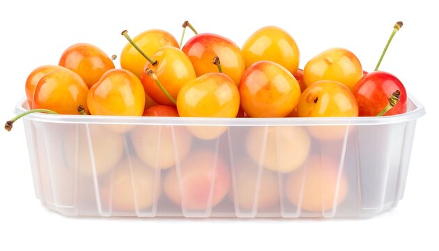 A close-up shot of a plastic container overflowing with golden-yellow cherries. Some have a blush of red, stems attached