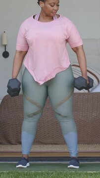 Vertical video: Shifting, woman in pink top doing hinge row at door with hex dumbbells for strength