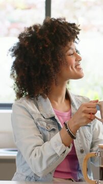 Vertical video: Smiling woman in denim seeing friend entering kitchen clinking mugs by French press