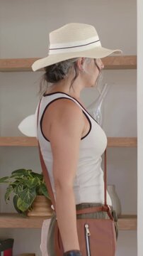 Vertical video: Adjusting woman in straw hat eyeing foyer doorway, sliding purse and preparing exit