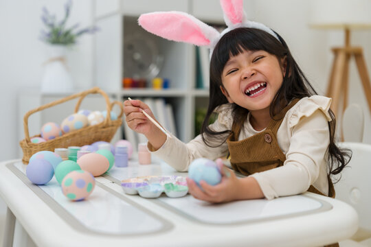 happy preschool child girl wearing bunny ears painting and decorating colorful egg at home on easter day
