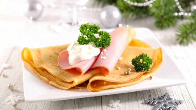 Savory breakfast crepes topped with thin ham slices and fresh cream garnish served on a white plate with festive Christmas decor