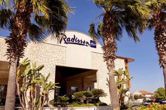 CESME, TURKEY - SEPTEMBER 20, 2025: The exterior facade of the Radisson Blu Resort & Spa in Cesme, featuring the hotel logo and tall palm trees under a clear blue sky