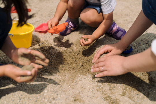 Children and adults play together in the sand, using buckets and shovels to build and create.