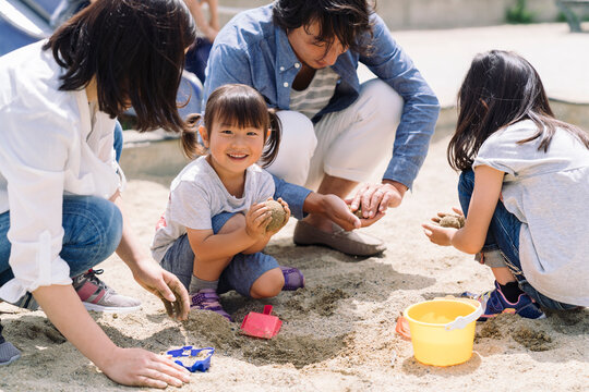 A family enjoys playing in the sand together, with parents and children building and digging in the sandbox.