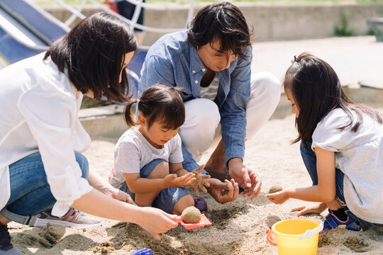A family plays together in the sand, with parents and children building and digging in the sandpit.