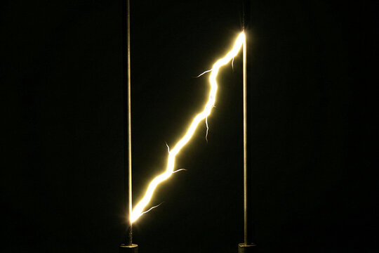 High voltage yellow electrical plasma arc traveling between two metal rods