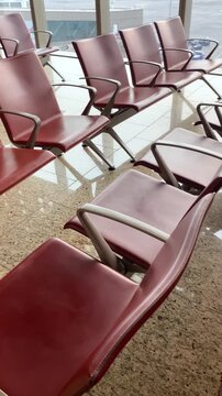 Red airport seating arranged in rows with modern design, showcasing polished granite floor and large windows allowing natural light to illuminate the waiting area