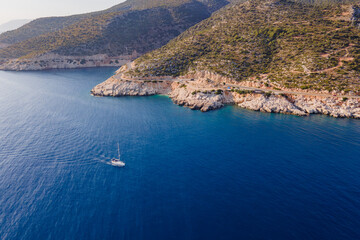 Fototapeta premium White sailboat cruising through blue sea along shore, aerial view