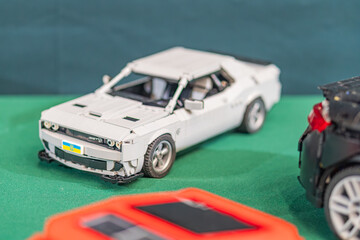 Fototapeta premium Two Lego toy cars on a textured, green-brown surface, with a white Lego car compact design, black tires, cockpit detail slightly ahead and a streamlined dark car t - Kyiv, Ukraine - June 7, 2025