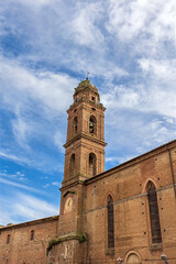 Obraz premium The Church of San Niccolo al Carmine shows its red brick structure under a blue sky. The tall bell tower features a clock. This site is part of Tuscany's architectural heritage in Siena.