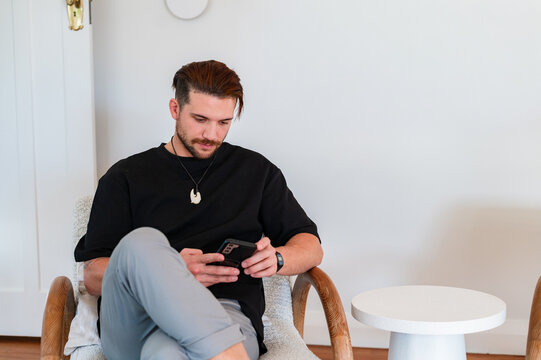 Man in black shirt sitting on a chair engaged on his phone inside home