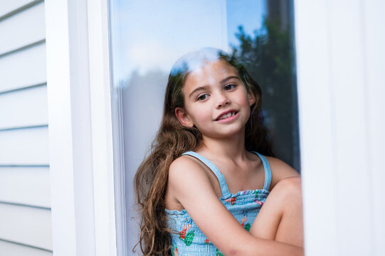 Young girl with long hair sitting on the windowsill inside the house