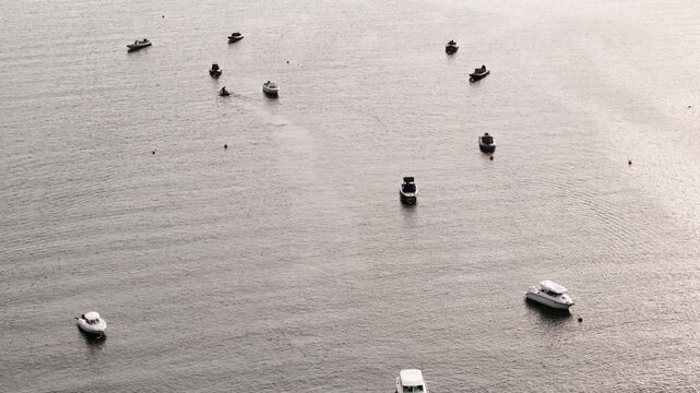 An aerial perspective shows many different boats and small vessels floating at rest on the wide, calm water of a bay.