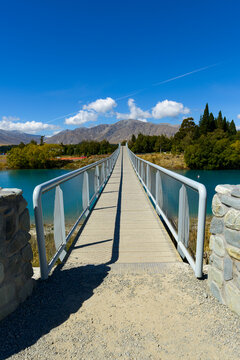 leading lines of railings and sharp shadows on a walking bridge over water with mountain