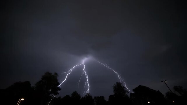 A dramatic bolt of lightning illuminates the dark, stormy sky above silhouetted trees and a streetlamp.