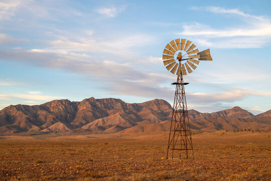 A rustic outback windmill stands before a dramatic mountain range on an arid plain