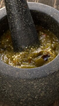 Roasted tomatillo salsa with dried and toasted chilies de arbol in a molcajete. Typical Mexican dip. Zoom in while totating. Vertical video.