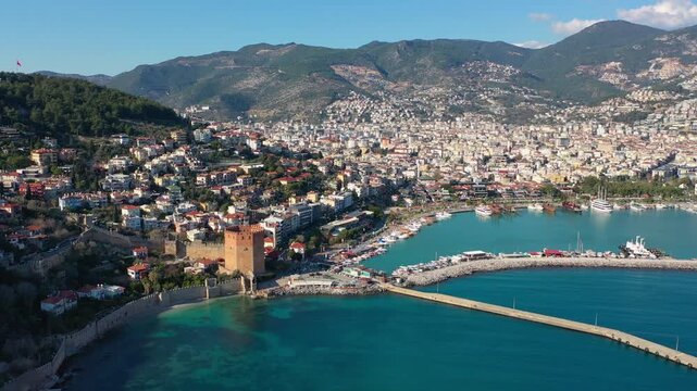 Aerial view of the historic Red Tower (Kızıl Kule), medieval shipyards and Alanya Marina along the turquoise Mediterranean coast in Alanya, Turkey, capturing harbor architecture.