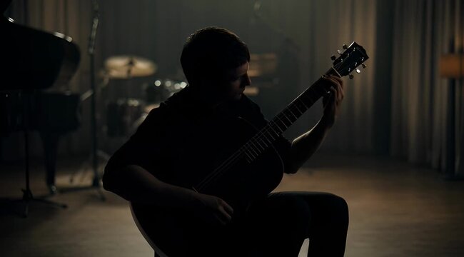 Silhouette of a musician playing acoustic guitar in a dimly lit studio