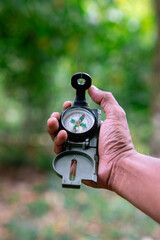 Naklejka premium A hand holds an antique compass outdoors. A green forest is faintly visible behind it.