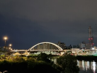 Naklejka premium Modern illuminated arch bridge over a city river at night