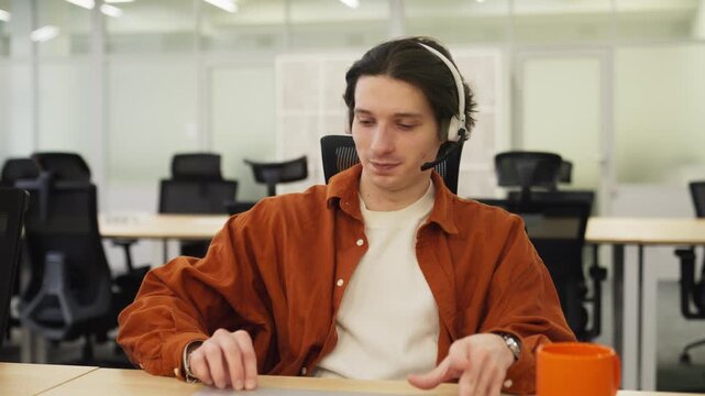 Caucasian operator taking off headset after work in office. Sitting at desk and consulting customer through laptop. Closing his laptop after work. Getting relief