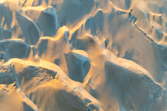 Aerial close-up of sculpted sand dunes with golden light and shadow creating abstract patterns