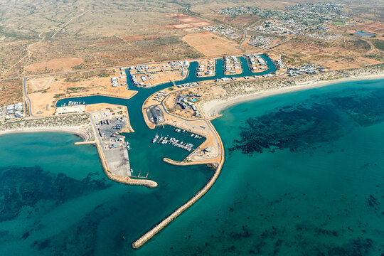 Aerial view of a coastal marina with boat moorings, breakwater and arid town beyond