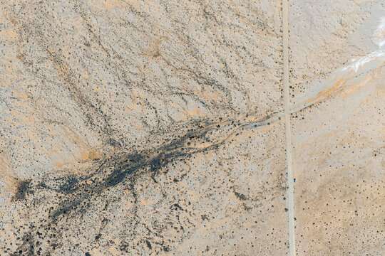 Aerial view of a straight dirt road crossing a dark, branching dry watercourse in the desert
