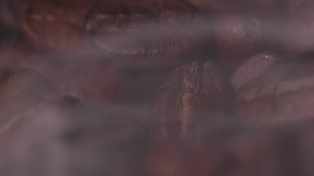 Roasted coffee beans releasing smoke on tabletop in studio kitchen, dark mood.
