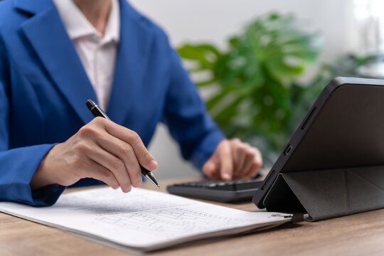 Close up of Asian female teacher hands holding pen while checking student exam papers,Recording scores on tablet and uploading academic data to central online system, Fast digital education management