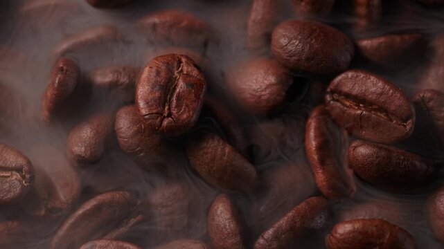 Macro process of roasting coffee beans with smoke on dark background, sliding shot top view.