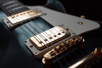 A guitar rests on a wooden table with soft light highlighting its body and strings. Knobs and switches catch the light. The room has a warm atmosphere as music fills the air