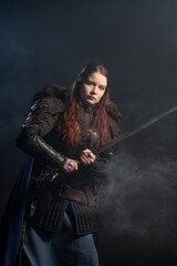 Fototapeta premium A fierce warrior woman with fiery hair and armor holds a sword amidst swirling smoke.