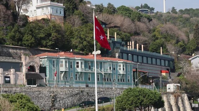 Traditional turquoise Ottoman Yali wooden mansion on Bosphorus in Istanbul and a prominent turkish national flag under a clear sky.