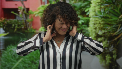 Woman in striped shirt grimaces while covering ears with hands in lush green forest clearing  annoyance. © Krakenimages.com