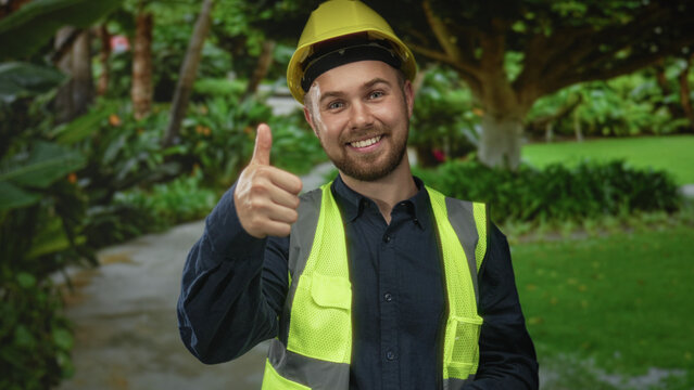 Man in hardhat and reflective vest giving thumbs up with hand near ear in forest; confidence teamwork.