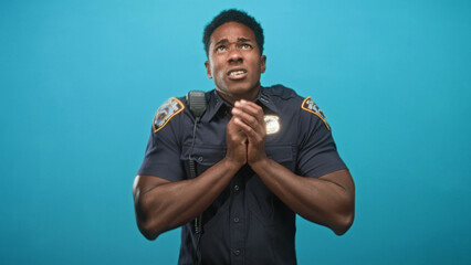 African american police officer man with hands clasped at chest and looking upward in studio;...