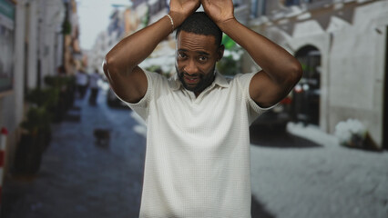 Naklejka premium Man with hands above head and palms raised on street wearing white polo shirt, smiling toward camera; playful moment.