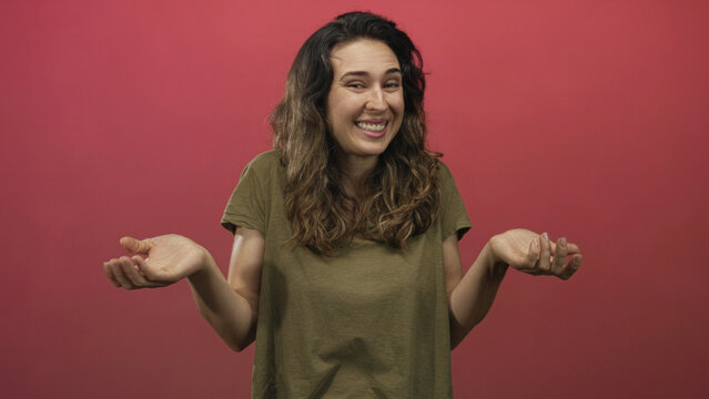 Woman in olive shirt shrugs arms with raised shoulders in studio with red background; quiet uncertainty.
