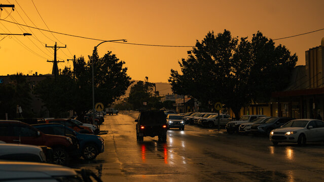 Vehicles driving along street in small town during sunset thunderstorm
