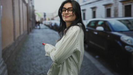 Fototapeta premium Woman extends both hands backward against a historic stone building facade on narrow street; invitation.