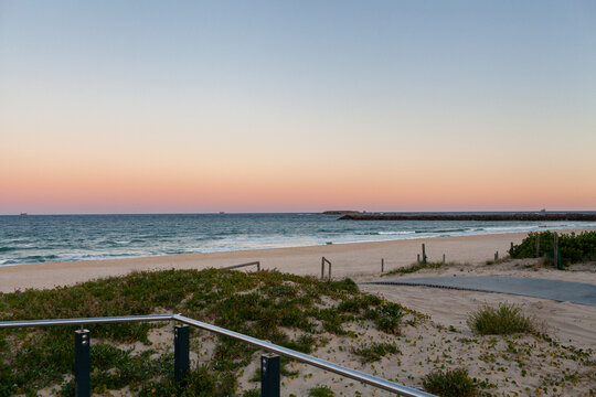 Sand dunes and railing to beach and ocean with dusk colour gradient in evening sky