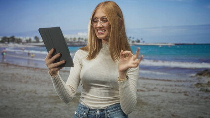 Redhead woman wearing glasses and sweater, holding a tablet, hand tapping screen while smiling in a...